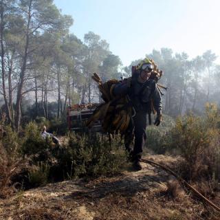 Un bomber carrega una mànega per pujar fins al cap del foc, a Foixà