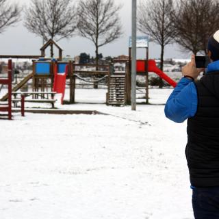 Un home fent una foto amb el mòbil als seus fills que juguen amb la neu al parc de l'Ondara a Tàrrega