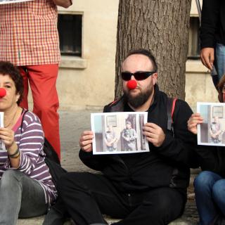 Persones assegudes davant la fiscalia de Tarragona amb nas de pallasso i cartells amb la imatge de Jordi Pesarrodona al costat d'un guàrdia civil