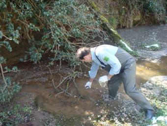 Un agent rural recollint mostres d’aigua contaminada de la riera on van abocar els purins