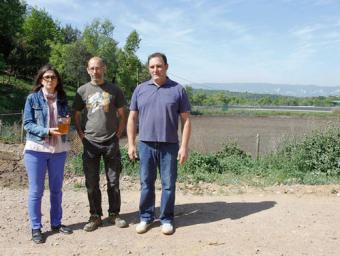 Noemí Cuenca, amb un pot amb l’aigua ja depurada; Marc Garriga, i Josep Masramon, propietari d’El Bruguer, davant la bassa amb tot el purí que es tran Sagi Serra