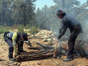 Dos bombers retiren soques que encara cremen, per evitar la revifada del foc d'Horta de Sant Joan. ACN