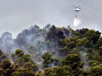 Un helicòpter llança aigua per evitar la propagació del foc. EFE