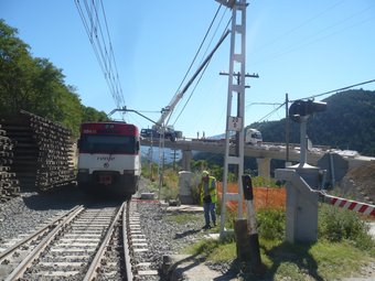 Un tren a punt de passar per sota de l'estructura del viaducte que es construeix a tocar de l'estació de Planoles. J.C