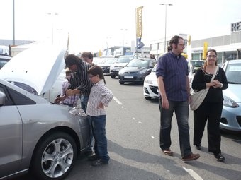 Un família mira el motor d'un dels cotxes que estan en venda, mentre una parella passeja per la mostra. ANNA PUIG