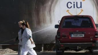 Dues treballadores passen per davant d'un cartell electoral de CiU, amb un cotxe aparcat al davant, ahir en un polígon de Tarragona. JOSÉ CARLOS LEÓN