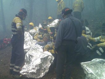 Un grup de bombers esperen que passi el foc envoltats de fum protegits amb mantes ignífugues en l'incendi d'Horta.