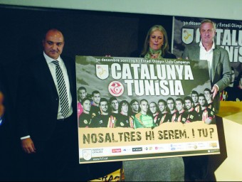 Subies (esquerra) amb Cruyff i Maite Fandos davant el cartell de presentació del partit del 30 de desembre. QUIM PUIG