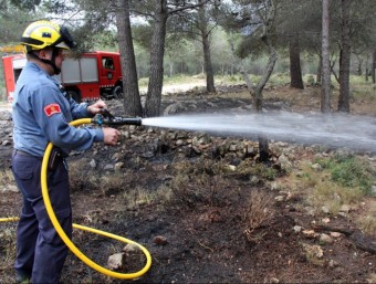 Els bombers voluntaris remullant la zona cremada ACN