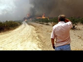Un llaurador observa amb preocupació com el foc s'aproxima als seus camps de conreu al terme municipal de Macastre. EFE/MANUEL BRUQUE