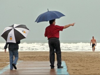 Un pare passeja amb el seu fill per la platja mentre un banyista surt de l'aigua. MANUEL BRUQUE - EFE