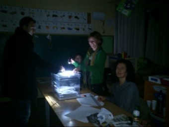 Un votant dipositant ahir la papereta mentre una de les membres de la mesa il·luminava l'urna amb un lot, a Santa Pau. Després, es van posar en funcionament generadors TURA SOLER