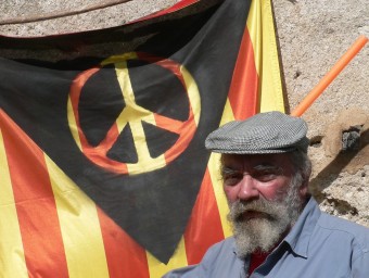 Lluís Hereu a casa seva a Vilobí davant la bandera confeccionada amb les quetre barres de Catalunya, el símbol de la pau i el triangle negre de l'anarquia. PAU LANAO