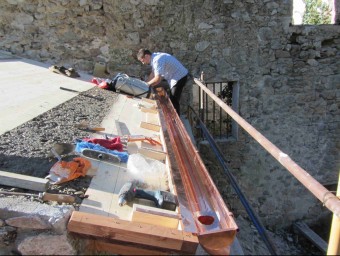 Un operari treballant en la col·locació d'una canal a la coberta de l'edifici annexe de l'antiga rectoria. AMICS DE SANT ANIOL D'AGUJA