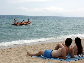 Dos banyistes observen des de la tovallola el pas de l'embarcació de la Creu Roja, en tasques de prevenció ACN