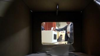 Una urna plena de paperetes, a través de la qual es veu un home votant el 9 de novembre QUIM PUIG