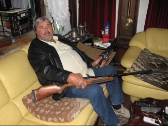 El veí de Calonge assaltat fa poc més d'un any, en una foto de fa pocs dies a la sala d'estar de casa seva amb una escopeta de balins i un ganivet de grans dimensions ÒSCAR PINILLA