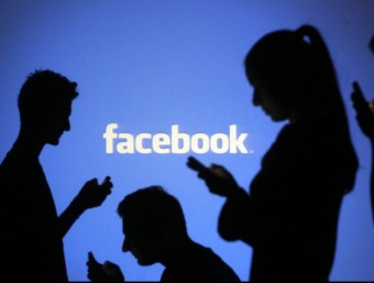 Silhouettes of people with mobile devices behind a screen projecting the Facebook logo  REUTERS