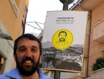 El candidat de CiU a Sant Hilari Sacalm, Albert Santaugini, amb un dels seus cartells, ahir a la plaça de l'Església QUIM PUIG