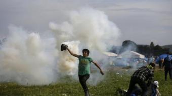 Un refugiat allunya una bomba de gasos llançada per la policia macedònia, aquest diumenge al campament d'Idomeni