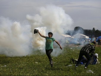 Un refugiat allunya una bomba de gasos llançada per la policia macedònia, aquest diumenge al campament d'Idomeni