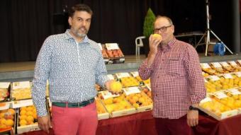 L'alcalde d'Alfarràs, Kleber Esteve (esquerra), i el productor Josep Maria Tomàs, davant d'un estand d'exposició de préssecs. E.BUSOMS/ACN